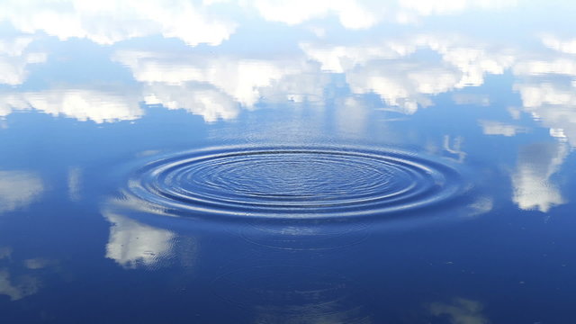 circles flow along surface of water, in water reflects sky with clouds
