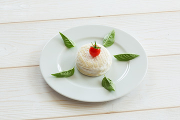 Camembert round cheese with cherry tomatoes and basil on a round white plate.