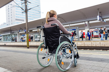 Frau sitzt in einem Rollstuhl auf einem Bahnhof