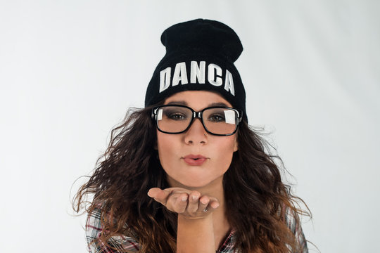 Portrait of young beautiful brunette dancer girl wearing glasses and black hipster hat sending blow kiss