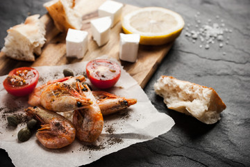 Fototapeta na wymiar Grilled shrimps on the peace of paper with different snack on the black stone table horizontal