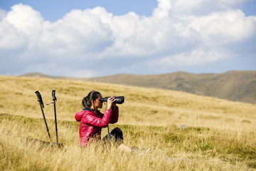 Hiker looking in binoculars enjoying spectacular view on mountai