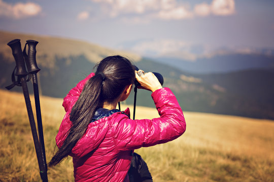 Hiker looking in binoculars enjoying spectacular view on mountai