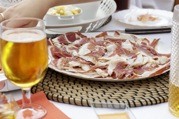 Dish of iberian ham slices beside beer glass and other foods