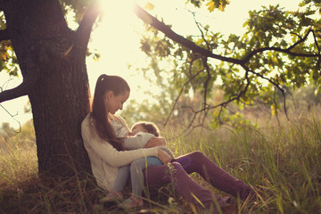 young mother feeding toddler under the tree