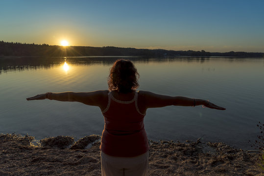Junge Frau beim Yoga macht Sonnengruß bei untergehender Sonne