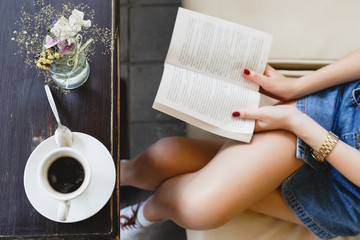 Young girl sitting on beige leather sofa and reading a book