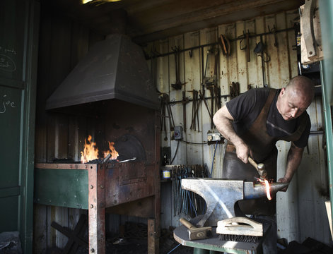 Blacksmith shaping a hot piece of iron on an anvil in a traditional forge with an open fire. 