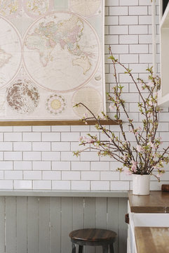 A kitchen worksurface, vase of flowers and a tiled wall. 