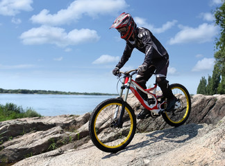 Naklejka na ściany i meble Sportsman in sportswear on a mountain bike rides on the stones in the extreme style of downhill