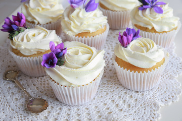 Edible purple freesia flowers on vanilla cupcakes with whipped c
