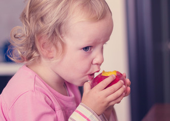 Funny little girl (2 years) eat a peach.