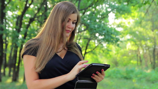 Beautiful young woman in a park on the tablet reads the Internet