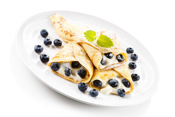 Crepes with blueberries and cream on white background