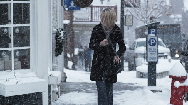 woman walking down a snowy street looking in her purse for something