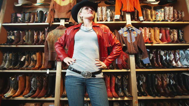 woman trying on a leather jacket and a cowboy hat at a western store