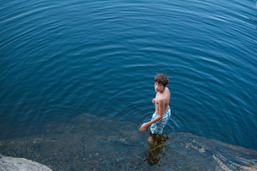 Fototapeta premium young boy wearing a bathing suit standing in a lake looking up at the camera