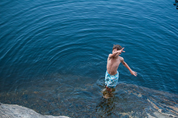 young boy wearing a bathing suit standing in a lake looking up at the camera