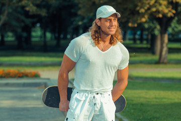 muscular long-haired guy in sunglasses with skateboard. Urban scene. Outdoor lifestyle portrait