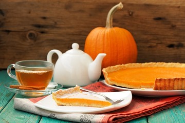 Tasty homemade pumpkin pie with cut piece, tea in glass cup, whi