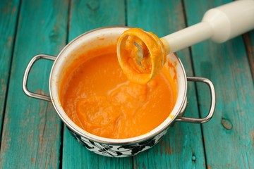 Tasty creamy pumpkin soup mixed with blender in white pot on tur