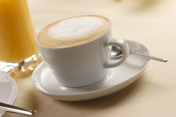 Fototapeta premium a cup of cappuccino and a glass of orange juice in the background