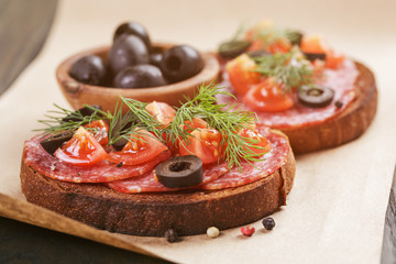 rye sandwich with salami and tomatoes on wood table