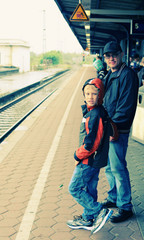Father and 7 years old boy standing on a railway station and wai