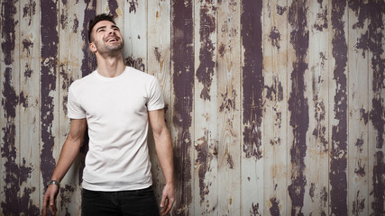 Smiling man in blank t-shirt, grunge wooden wall background