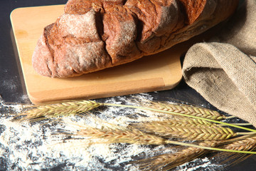 rustic crusty bread and wheat ears on a dark wooden table