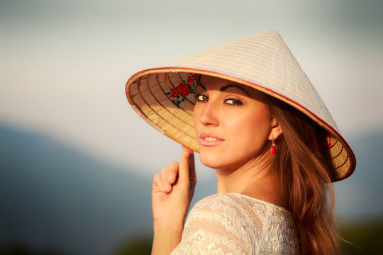 portrait of blonde girl in white Vietnamese hat against blur sky