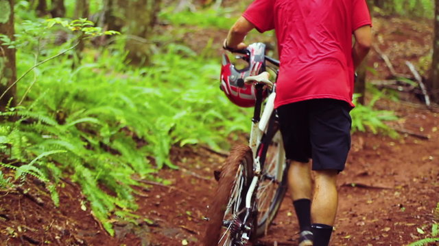 Young Man Walking Mountain Bike Uphill on Forest Trail.  Outdoor Sports Healthy Lifestyle. Slow Follow Shot with Steadicam. Summer Extreme Sports.