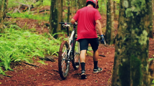 Young Man Walking Mountain Bike Uphill on Forest Trail.  Outdoor Sports Healthy Lifestyle. Slow Follow Shot with Steadicam. Summer Extreme Sports.