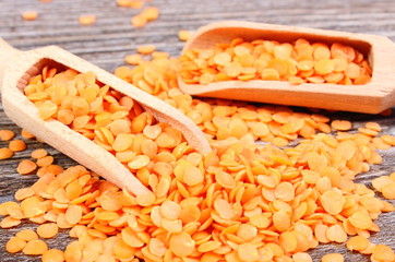 Heap of red lentil with spoon on wooden background