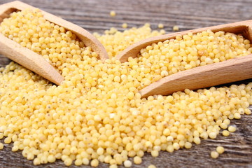 Heap of millet groats with spoon on wooden background