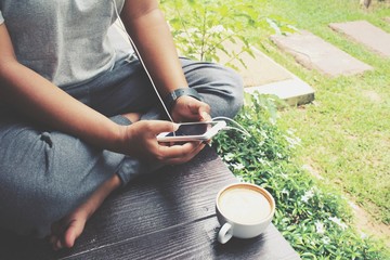 Woman playing smartphone with earphone and coffee in the garden