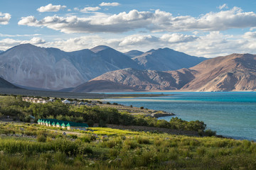 Fototapeta na wymiar Beautiful green field view at Pangong lake with some tents for tourist and mountain range background