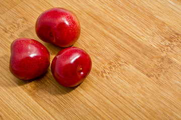 Dojrzałe czerwone owoce czereśni na desce.   Tło z kilkoma owocami czereśni na bambusowej kuchennej desce. © IreneuszB
