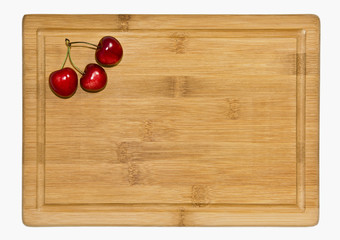 Dojrzałe czerwone owoce czereśni na desce.   Tło z kilkoma owocami czereśni na bambusowej kuchennej desce. © IreneuszB