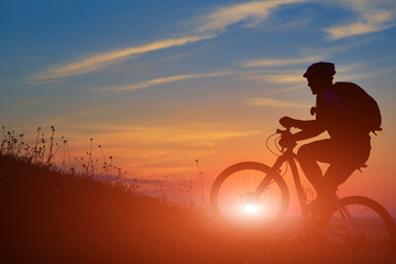 Silhouette of a biker and bicycle on sunset background.
