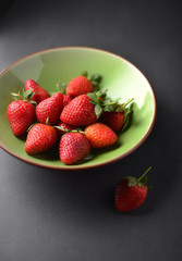 Fresh strawberries in a colorful bowl on dark background.