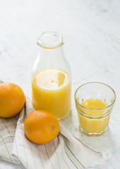 Orange juice. Half-filled bottle of fresh orange juice with whole oranges and glass of juice. morning breakfast table.