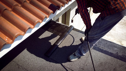 Roofer installing a roll of roofing felt by gas blowpipe torch