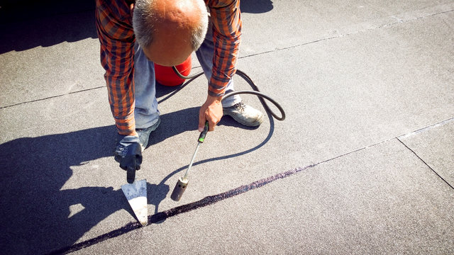 Roofer installing a roll of roofing felt by gas blowpipe torch