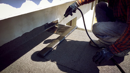 Roofer installing a roll of roofing felt by gas blowpipe torch