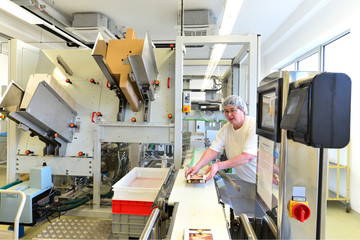 Frau an einer Verpackungsmaschine in einem Werk zur Herstellung von Pralinen und Süßwaren // Woman on a packaging machine in a factory for the production of chocolates and sweets