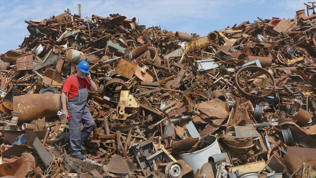Metal recycling, worker speaking by mobile phone at heap of scrap metal