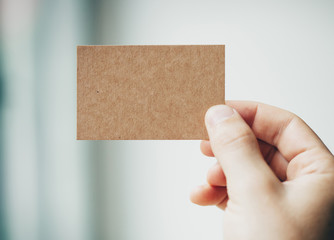 Male hand holding craft business card on the blurred background 