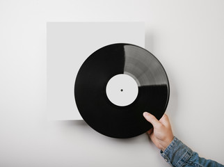 Male hand holding vinyl music album template on white wall backg