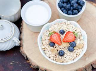 Breakfast in the garden: oatmeal cereals with berries on the dark wooden table, selective focus
